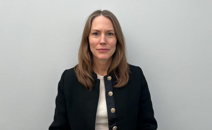 Kvinna i brunt hår, svart kofta och vit t-shirt.